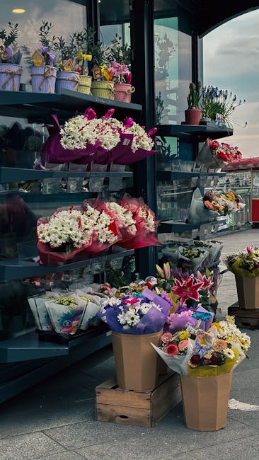 A display of fresh floral arrangements on dark blue shelving at Shepherds Bush Flowers, featuring a variety of bouquets including white chrysanthemums, pink lilies, and purple irises wrapped in colorf